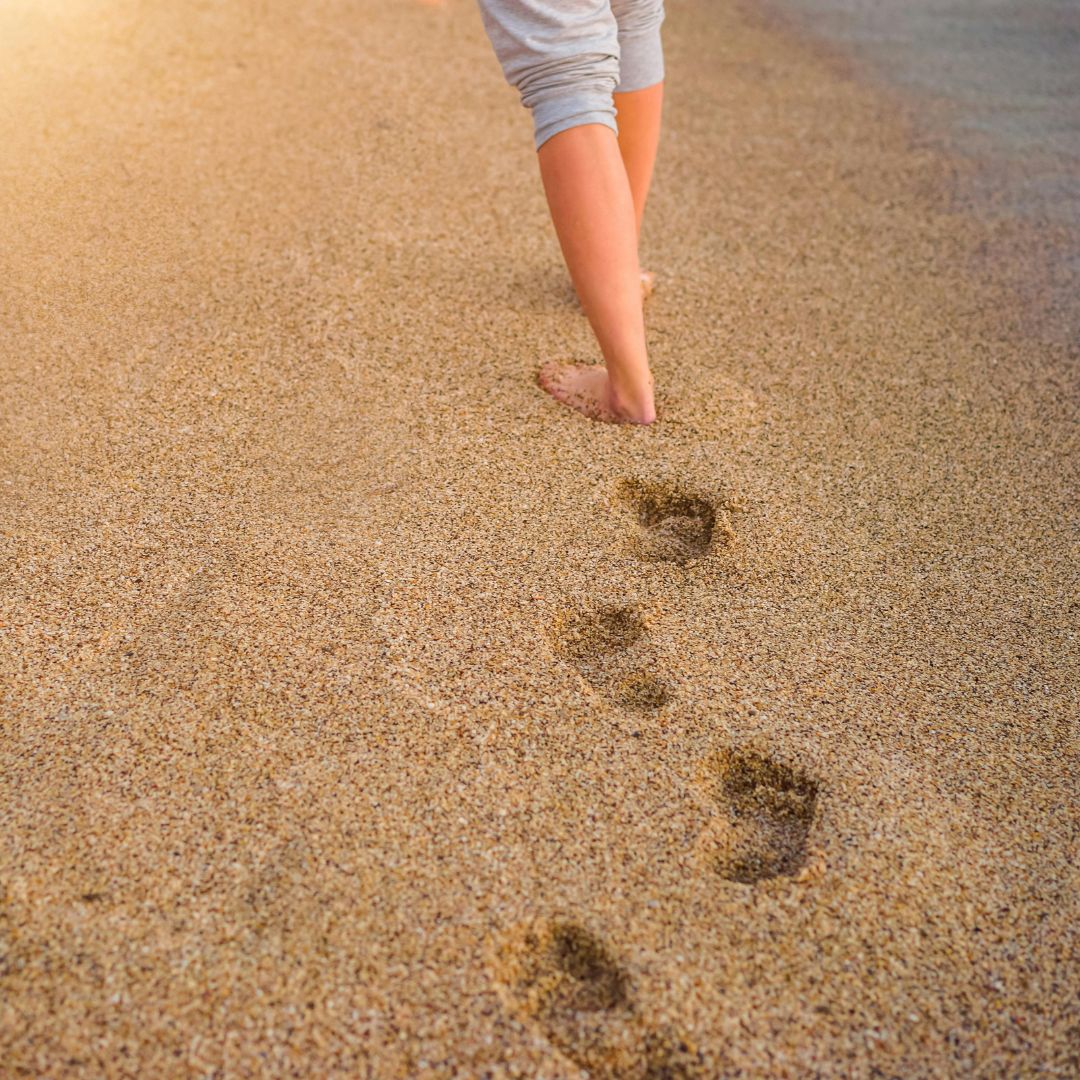 Askeleet ja kävelijän jalat rantahiekassa.